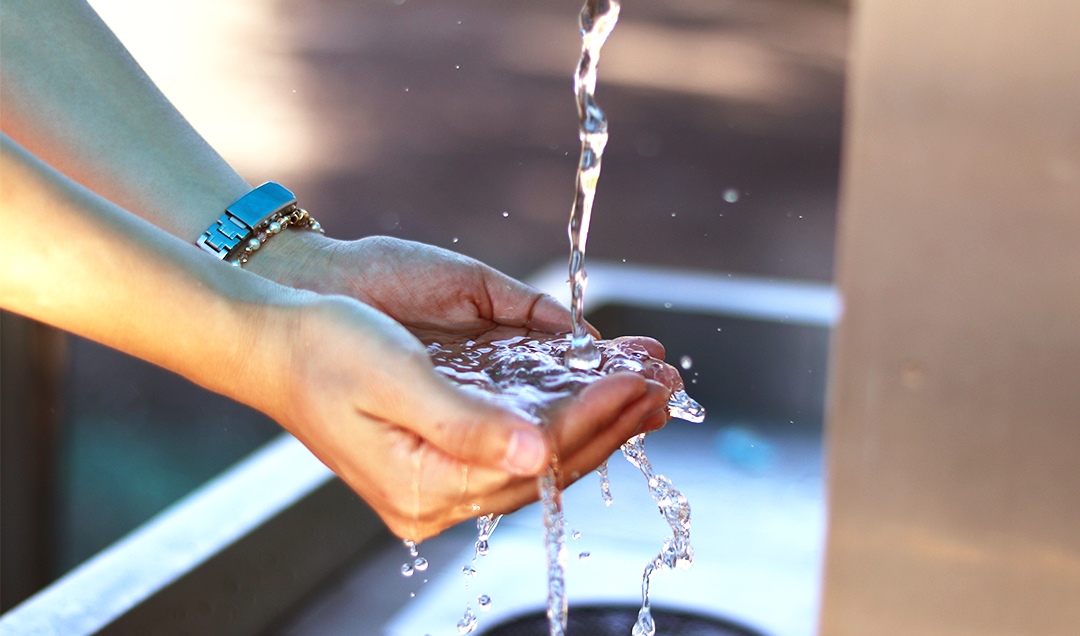 une femme tenant ses mains en coupe, contenant de l'eau venant d'un robinet en extérieur